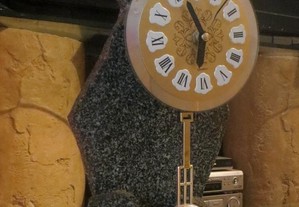 Relógio analógico, com mostrador em numeração, embutido em escultura esculpida em granito preto